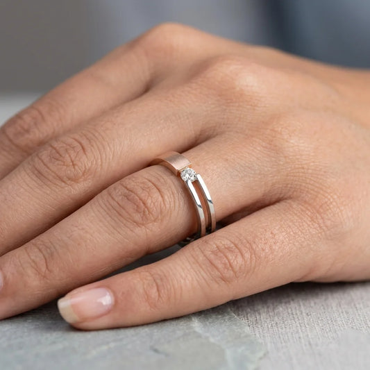Close-up of a hand wearing two tone gold and solitaire diamond ring on a neutral background