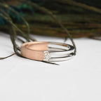 Two tone gold solitaire diamond ring, one rose gold and one white gold, on a white surface with a blurred natural background.