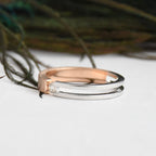 Two tone gold solitaire diamond ring, one rose gold and one white gold, on a white surface with a blurred natural background.