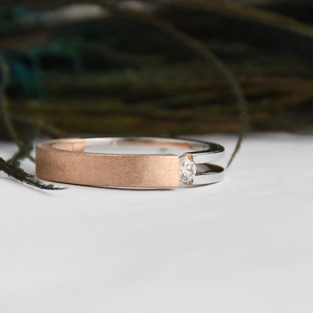Two tone gold ring with a diamond on a white surface