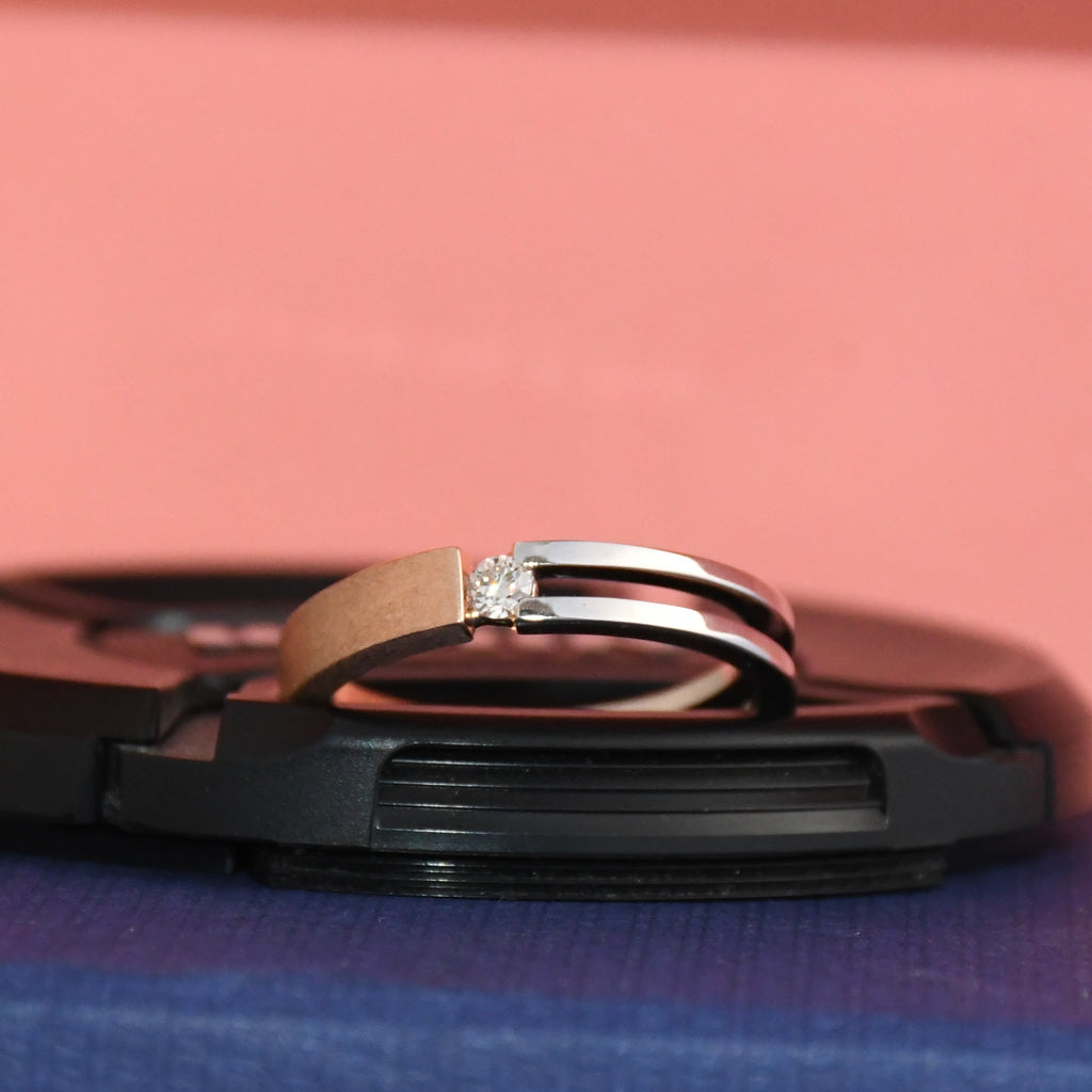 Two tone gold solitaire diamond ring on a black stand with a pink and blue gradient background
