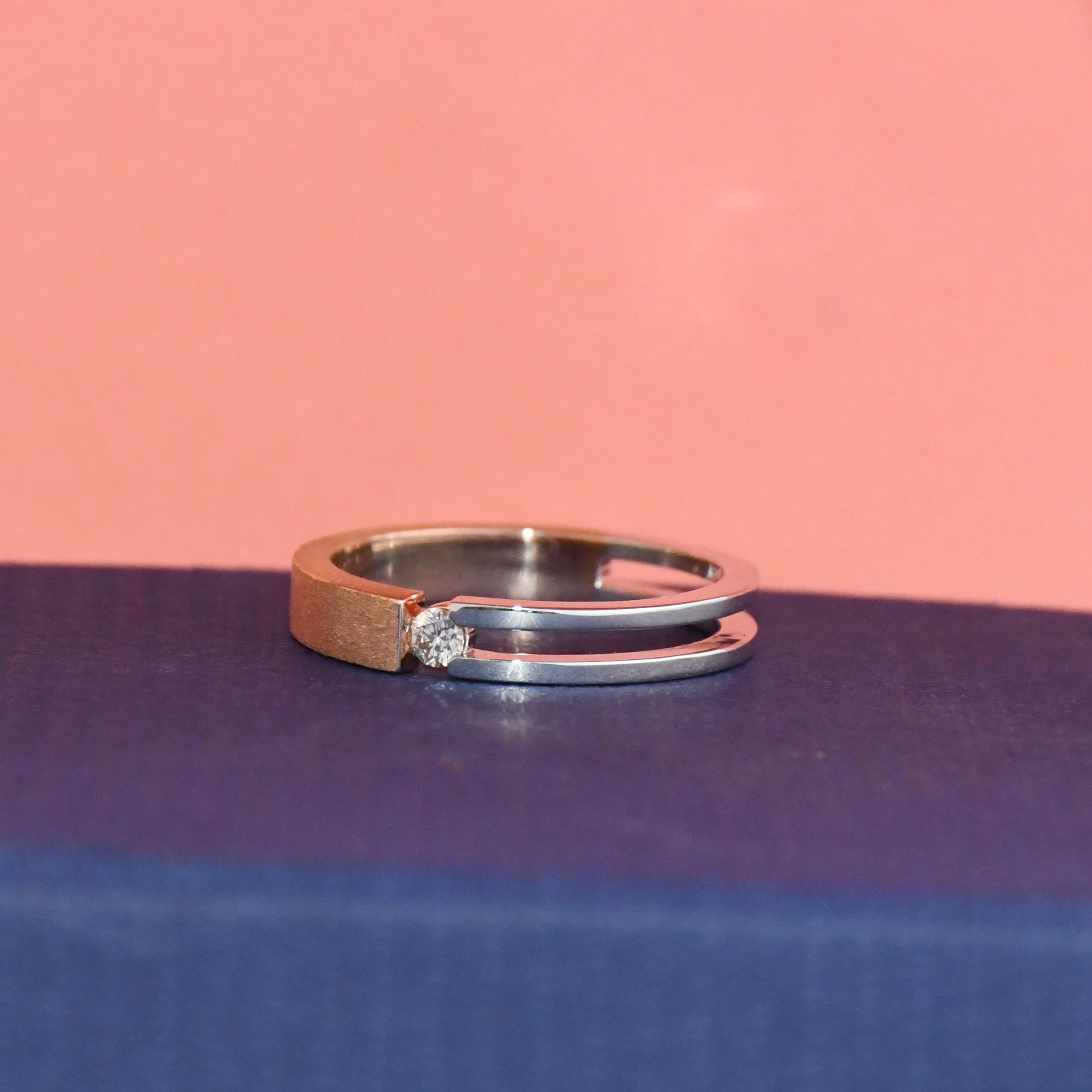 Two tone gold ring with a diamond on a blue and pink gradient background