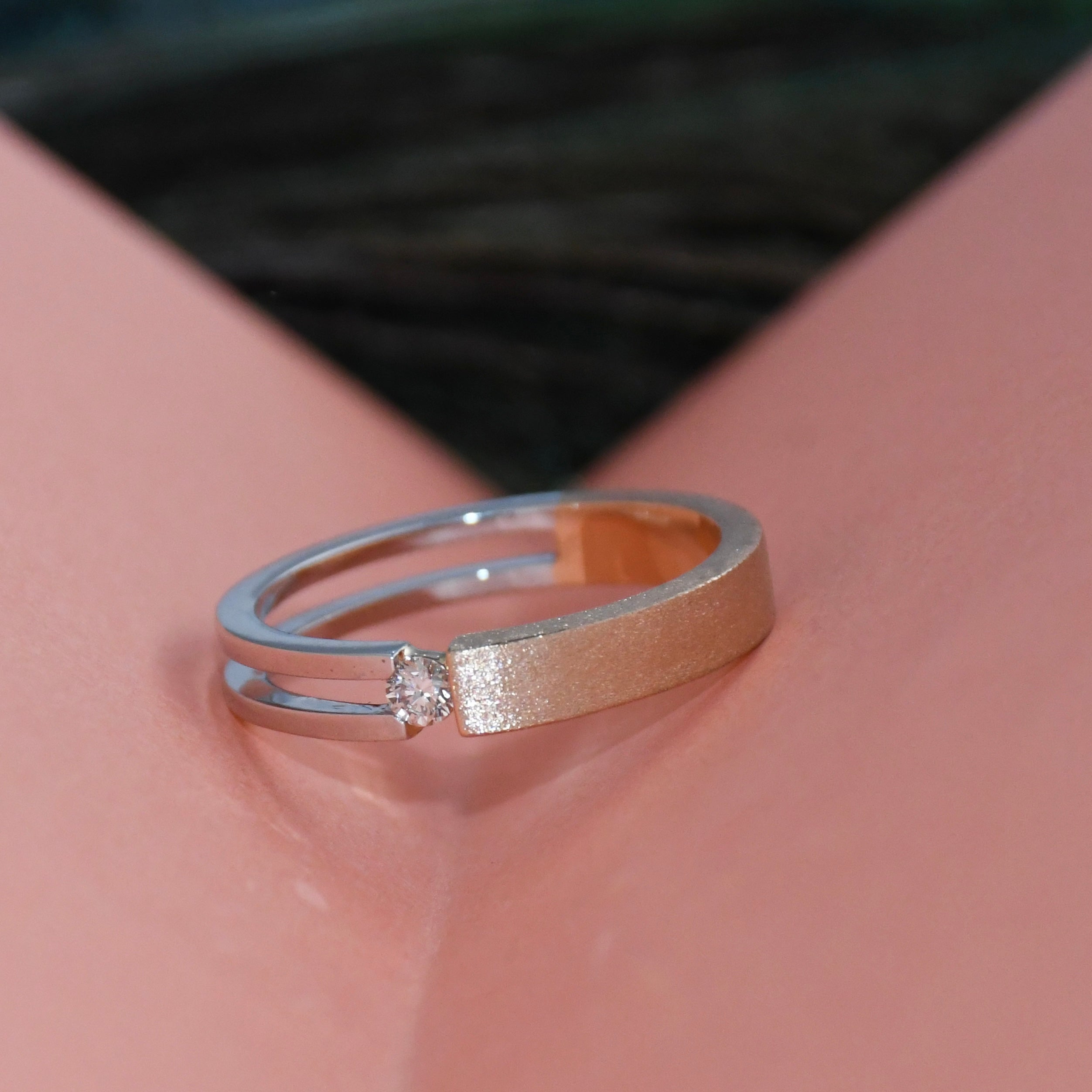 Two tone gold ring with a diamond on a pink folded paper.