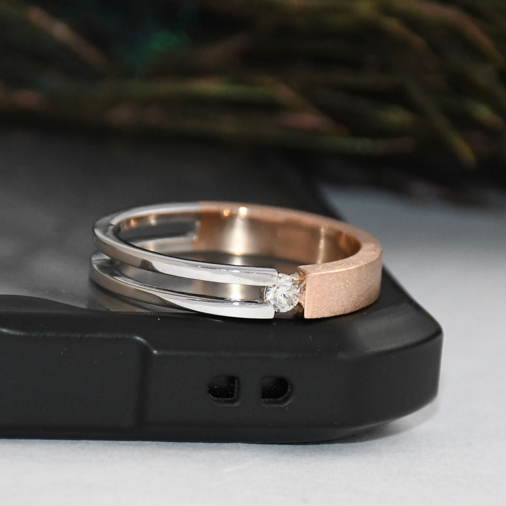 Two tone gold solitaire diamond ring stacked on a black surface with a blurred green background