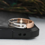 Two tone gold solitaire diamond ring stacked on a black surface with a blurred green background