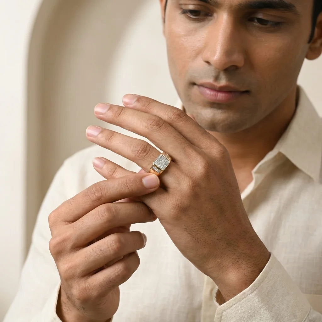 A gold ring with a square pavé diamond center and a small side channel of diamonds, holding by a men's finger against a neutral background.