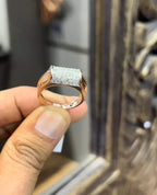 A man's hand holding a diamond men's ring with a gold band, featuring prominent diamonds centerpiece.