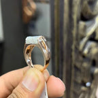 A man's hand holding a diamond men's ring with a gold band, featuring prominent diamonds centerpiece.