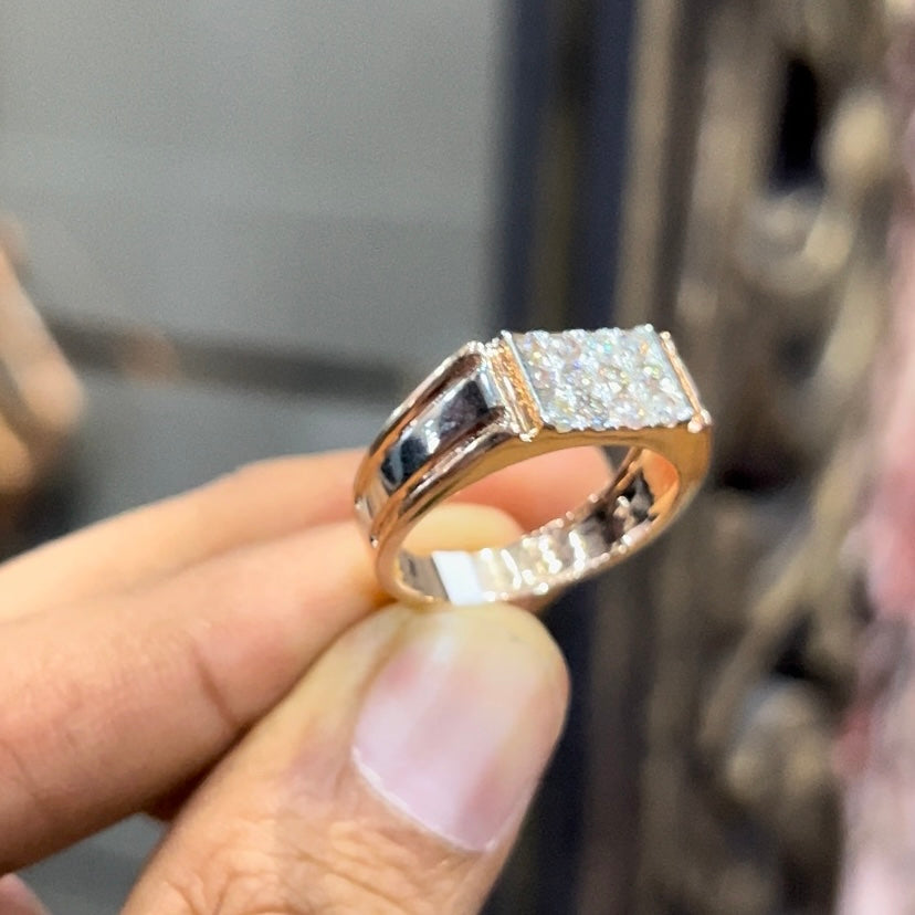Men’s diamond ring in dual-tone gold with bold rectangular cluster of round diamonds at the center, flanked by sleek metal panels, shown by a person's hand.