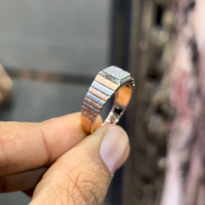 Stylish men’s diamond ring with a geometric square cluster centerpiece and textured rose gold band, shown in hand for scale.