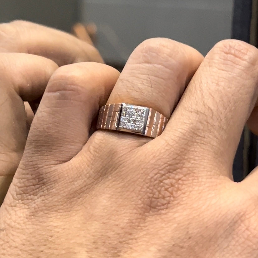 Stylish men’s diamond ring with a geometric square cluster centerpiece and textured rose gold band, shown in hand for scale.