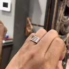 A man's hand displaying a diamond ring with a gold band. The ring has a polished finish with smaller diamonds.