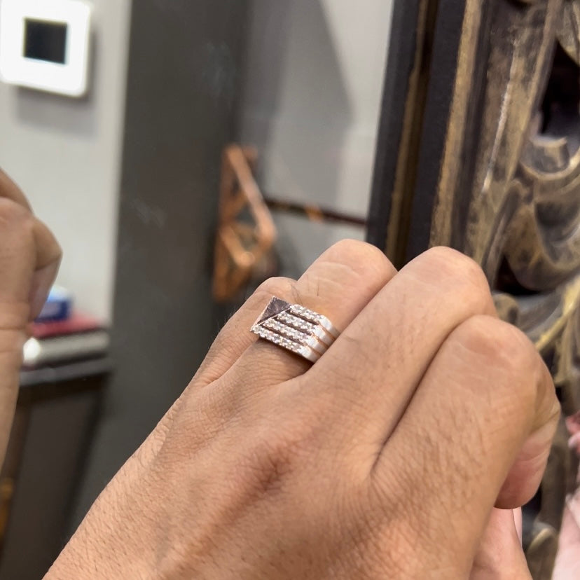 A man's hand displaying a diamond ring with a gold band. The ring has a polished finish with smaller diamonds.