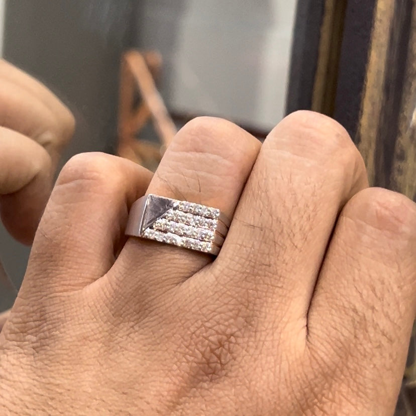 A man's hand displaying a diamond ring with a gold band. The ring has a polished finish with smaller diamonds.