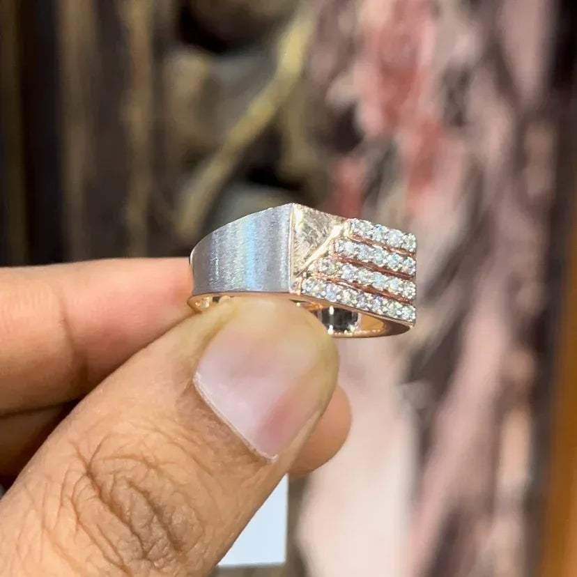 A man's hand displaying a diamond ring with a gold band. The ring has a polished finish with smaller diamonds.