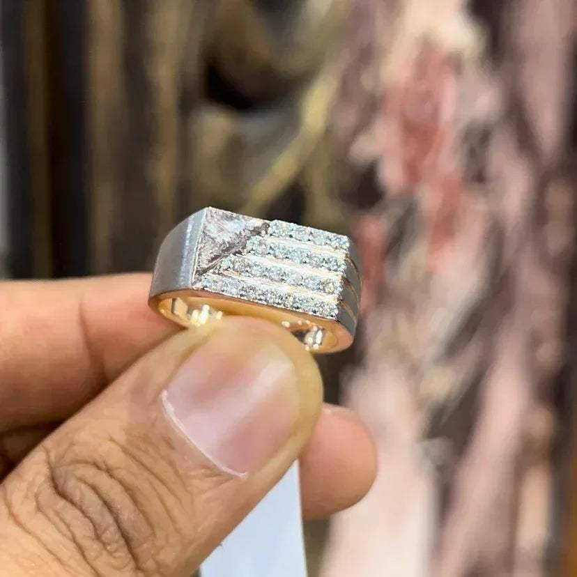 A man's hand displaying a diamond ring with a gold band. The ring has a polished finish with smaller diamonds.