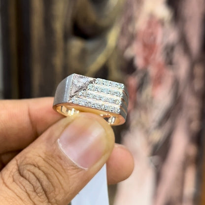 A man's hand displaying a diamond ring with a gold band. The ring has a polished finish with smaller diamonds.