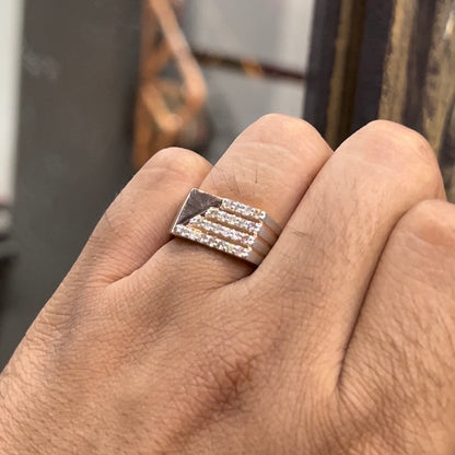 A man's hand displaying a diamond ring with a gold band. The ring has a polished finish with smaller diamonds.