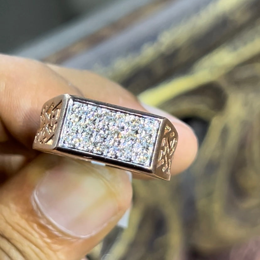 A man's hand displaying a diamond ring with a gold band. The ring has a polished finish with smaller diamonds.