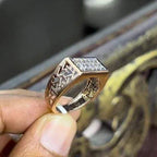 A man's hand displaying a diamond ring with a gold band. The ring has a polished finish with smaller diamonds.
