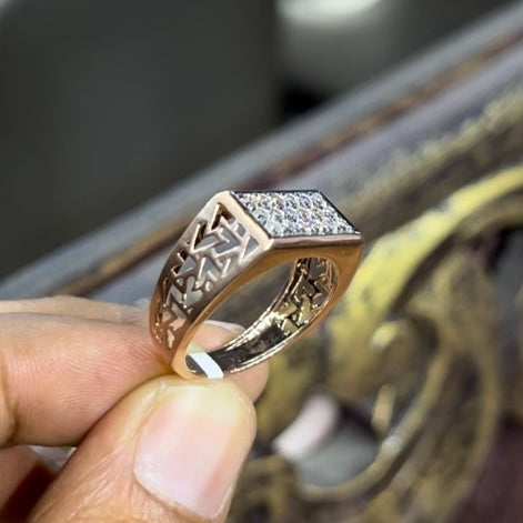 A man's hand displaying a diamond ring with a gold band. The ring has a polished finish with smaller diamonds.