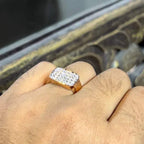 A man's hand holding a pave set diamond ring with a solid gold band, featuring a prominent smaller diamonds along the band.