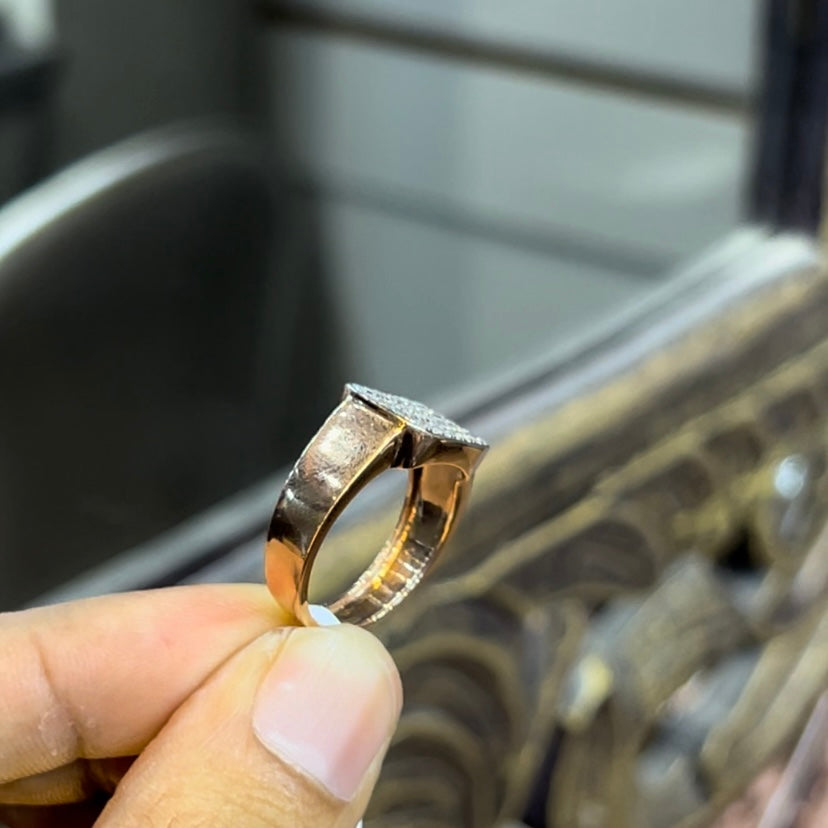 A man's hand holding a pave set diamond ring with a solid gold band, featuring a prominent smaller diamonds along the band.