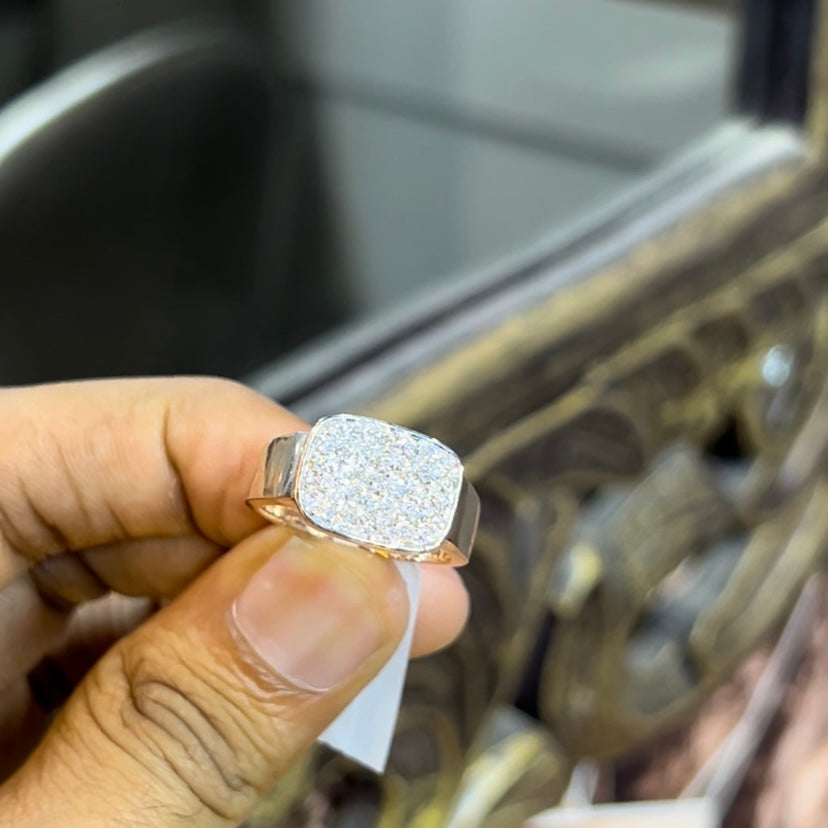 A man's hand holding a pave set diamond ring with a solid gold band, featuring a prominent smaller diamonds along the band.