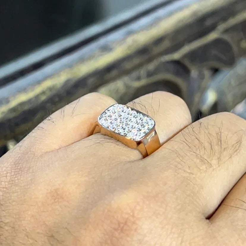 A man's hand holding a pave set diamond ring with a solid gold band, featuring a prominent smaller diamonds along the band.