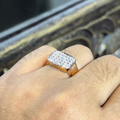 A man's hand holding a pave set diamond ring with a solid gold band, featuring a prominent smaller diamonds along the band.