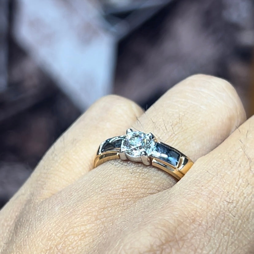 A man's hand holding a diamond solitaire ring with a gold ring.