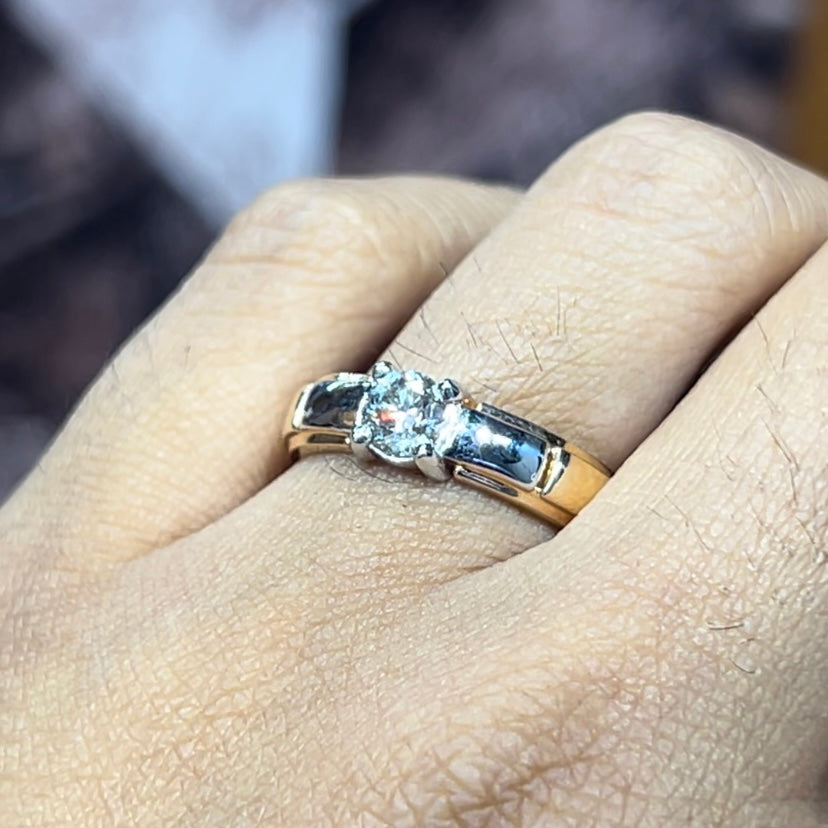A man's hand holding a diamond solitaire ring with a gold ring.