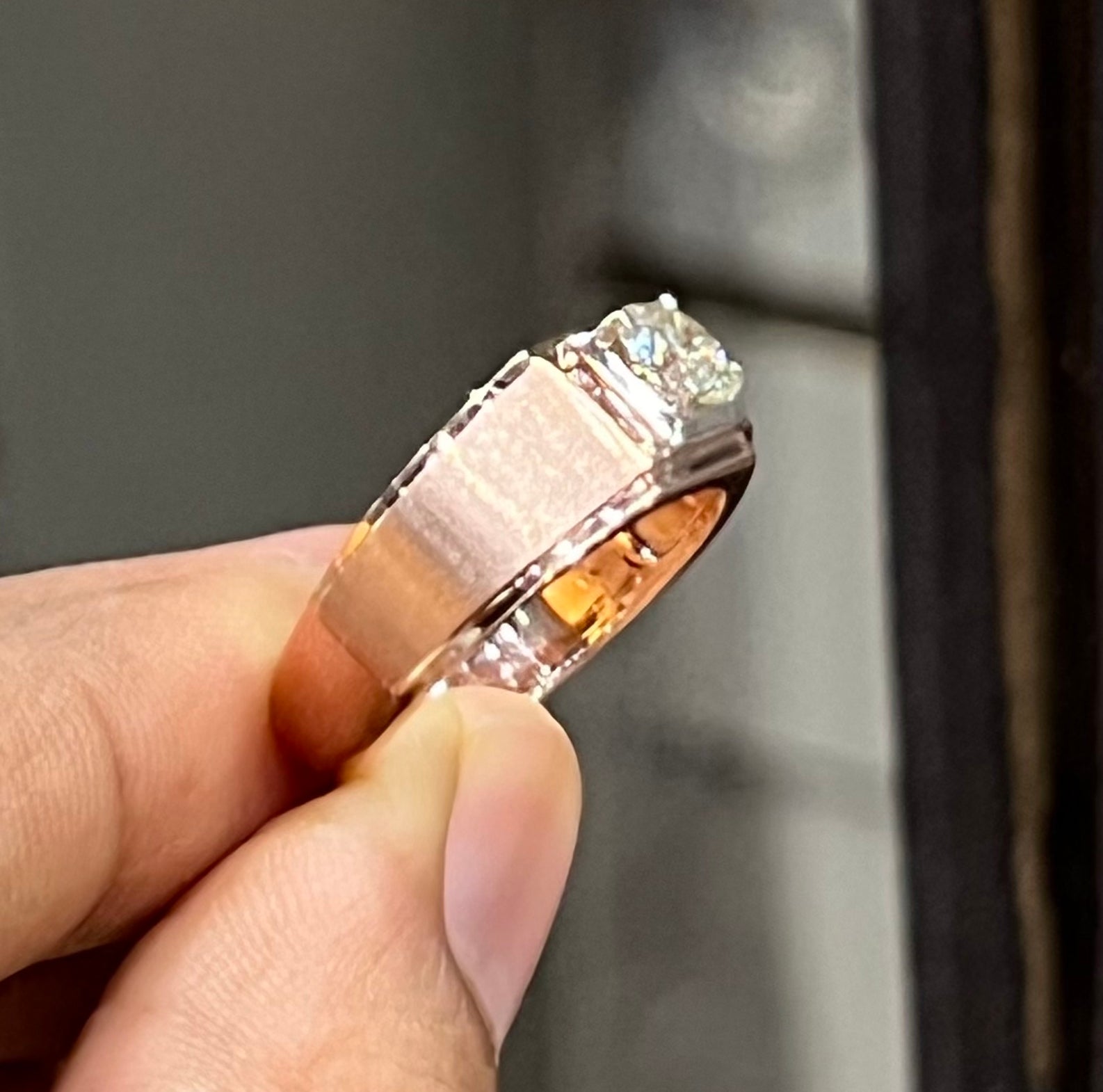 A man's hand displaying a solitaire men's diamond ring with a gold band.