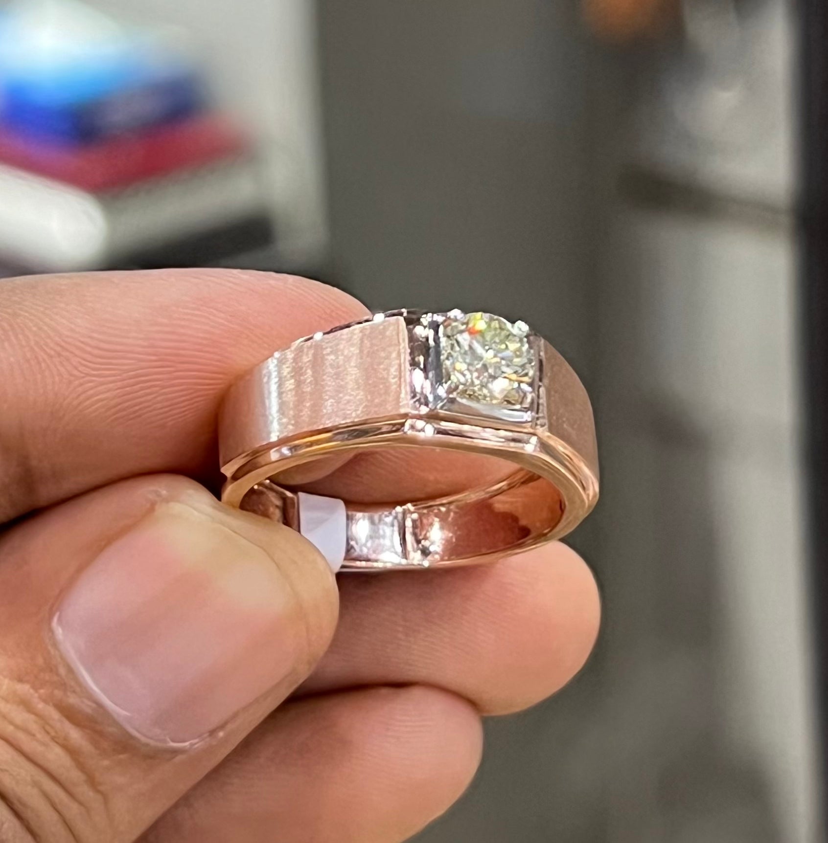 A man's hand displaying a solitaire men's diamond ring with a gold band.