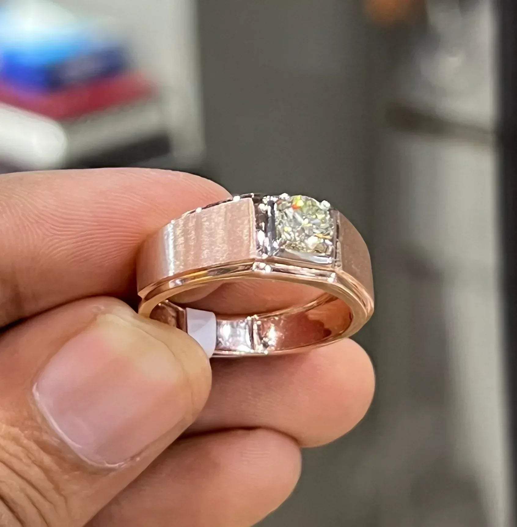 A man's hand displaying a solitaire men's diamond ring with a gold band.