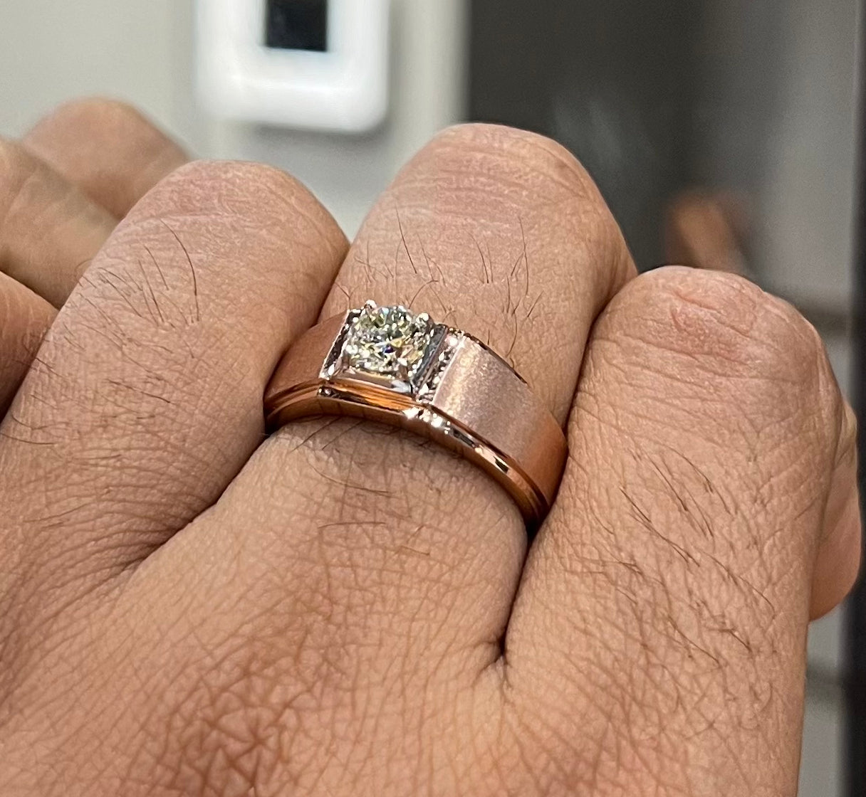 A man's hand displaying a solitaire men's diamond ring with a gold band.