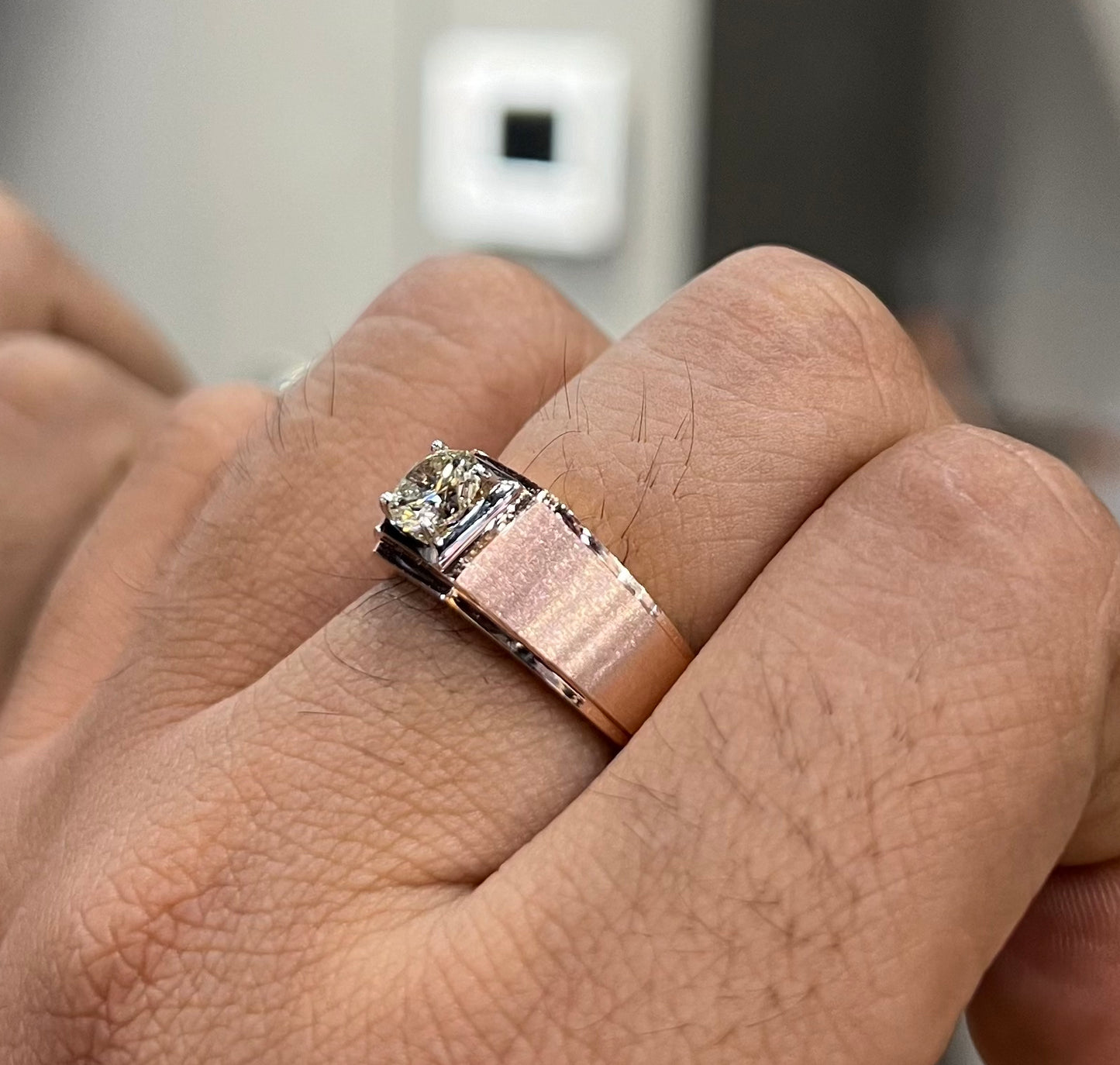 A man's hand displaying a solitaire men's diamond ring with a gold band.