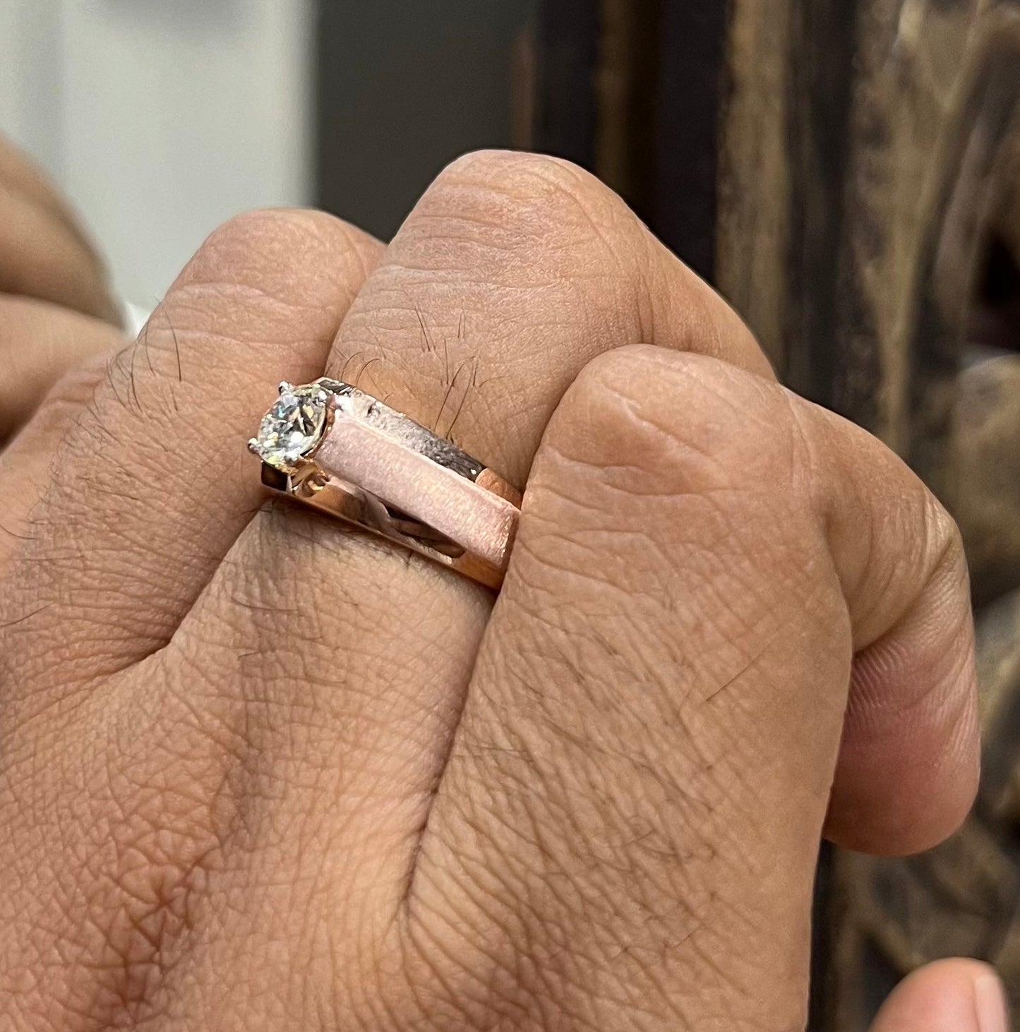 A man's hand displaying a gold band ring with a large, genuine diamond centerpiece.
