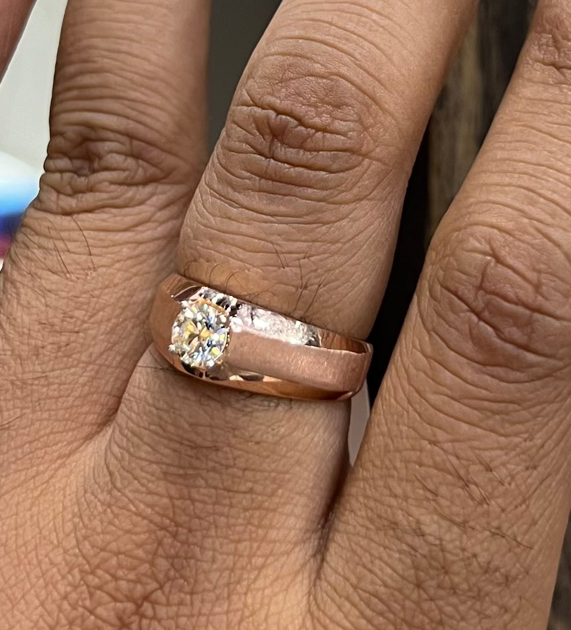 A man's hand displaying a gold band ring with a large, genuine diamond centerpiece.