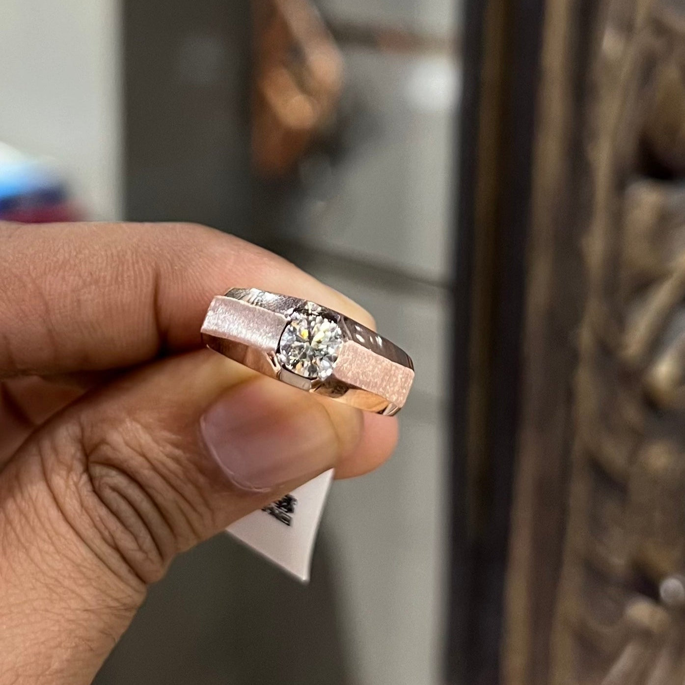A man's hand displaying a gold band ring with a large, genuine diamond centerpiece.