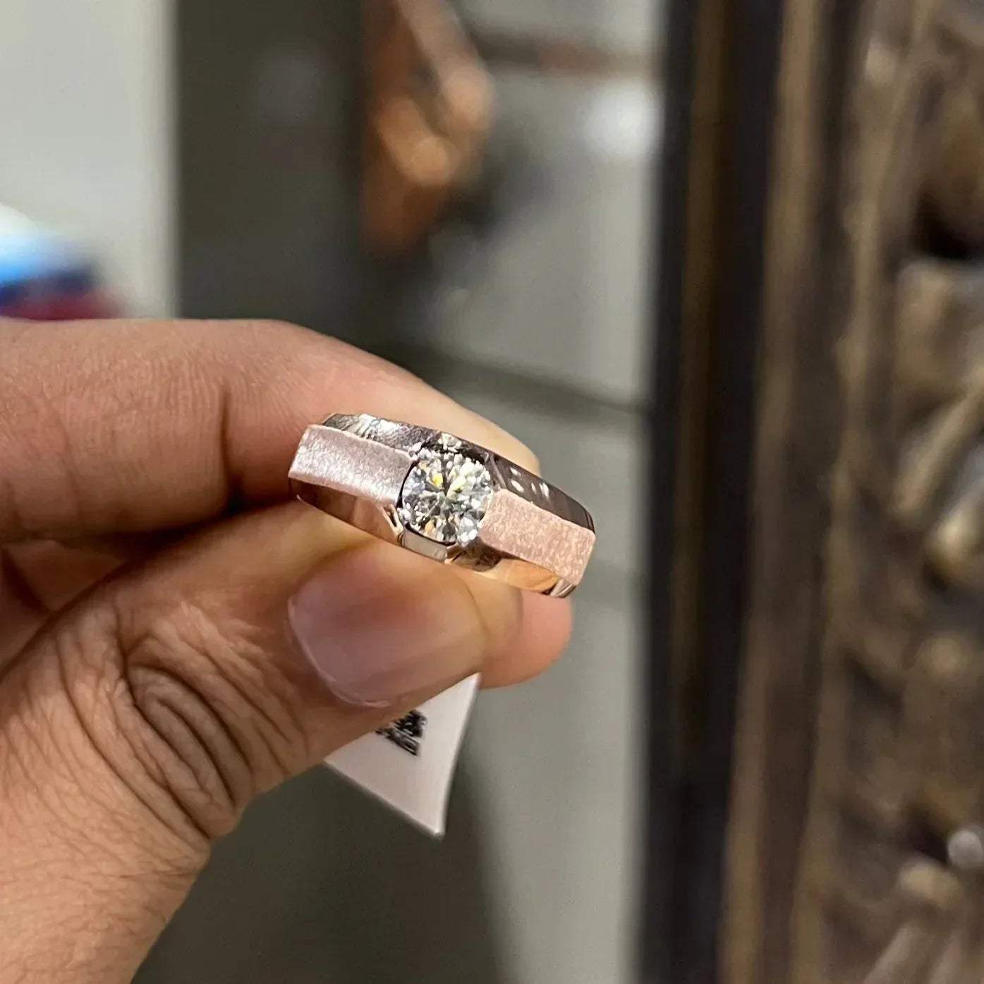 A man's hand displaying a gold band ring with a large, genuine diamond centerpiece.