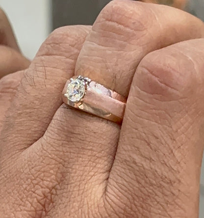 A man's hand displaying a gold band ring with a large, genuine diamond centerpiece.