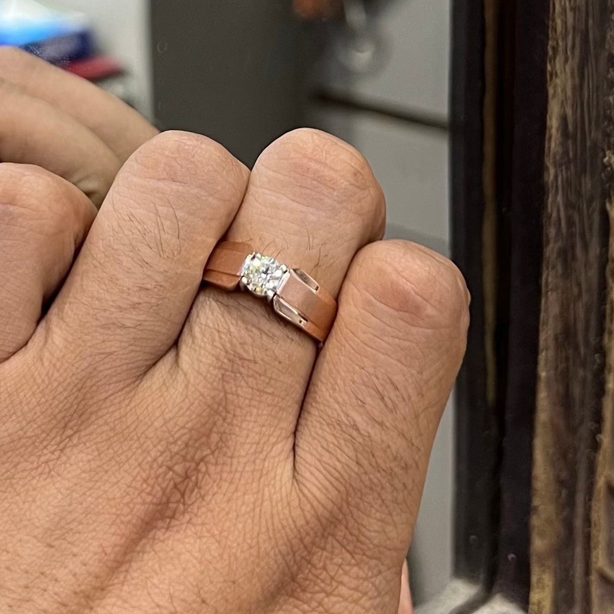 A man's hand holding a diamond solitaire ring with a gold band.