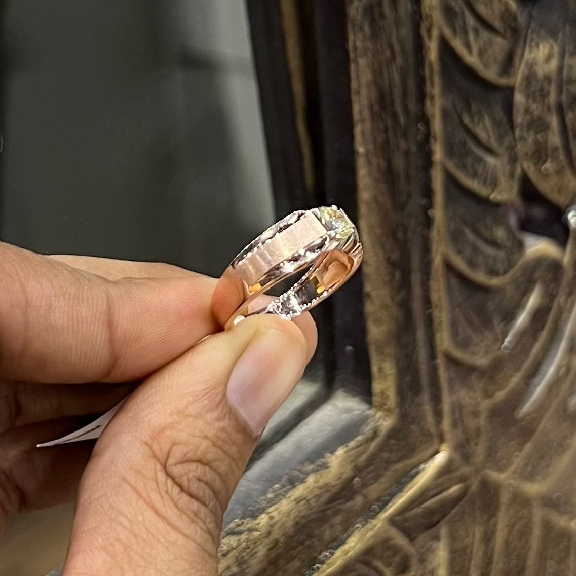 A man's hand holding a diamond solitaire ring with a gold band.