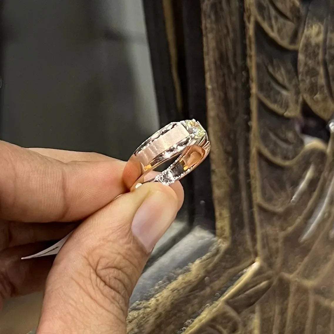 A man's hand holding a diamond solitaire ring with a gold band.
