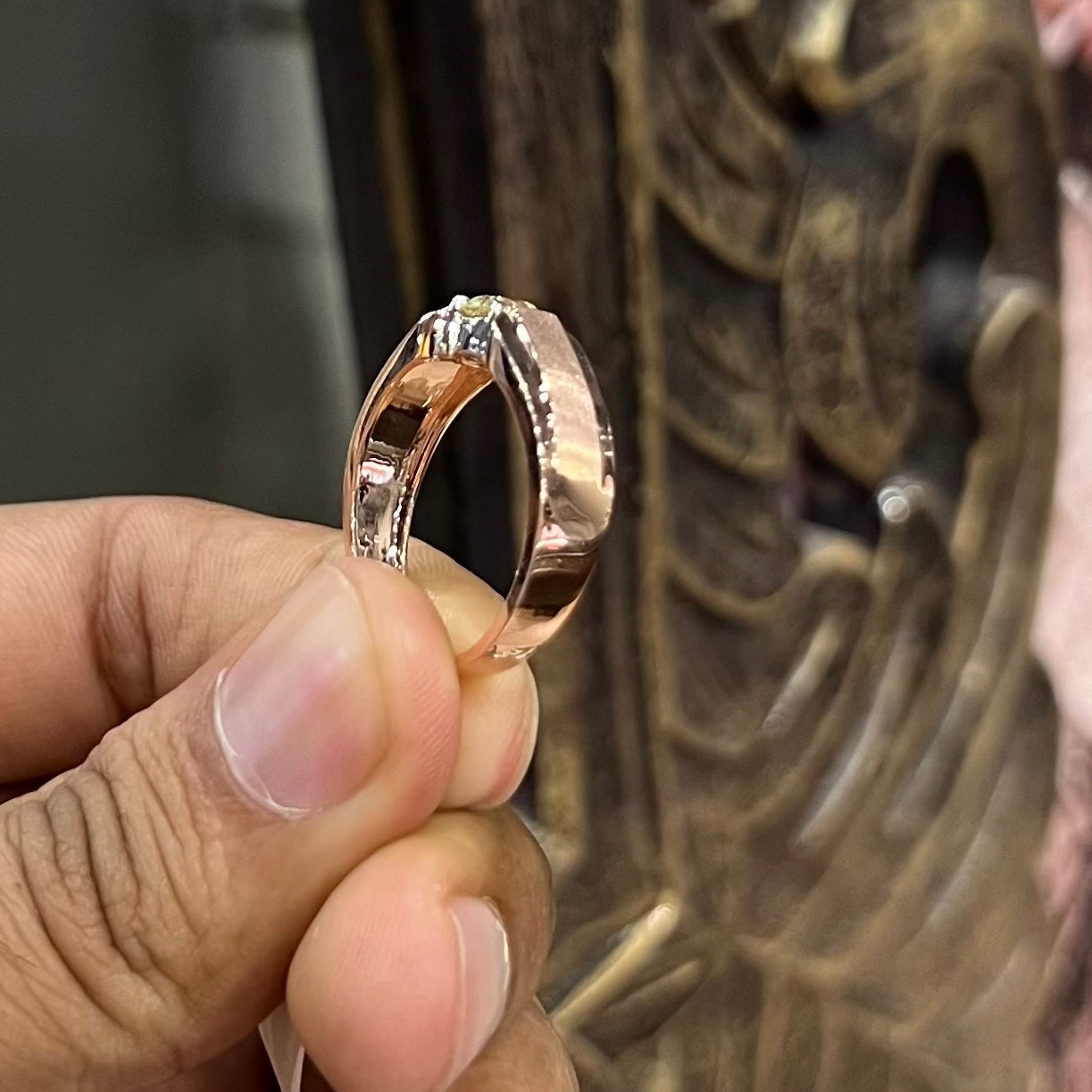 A man's hand holding a diamond solitaire ring with a gold band.