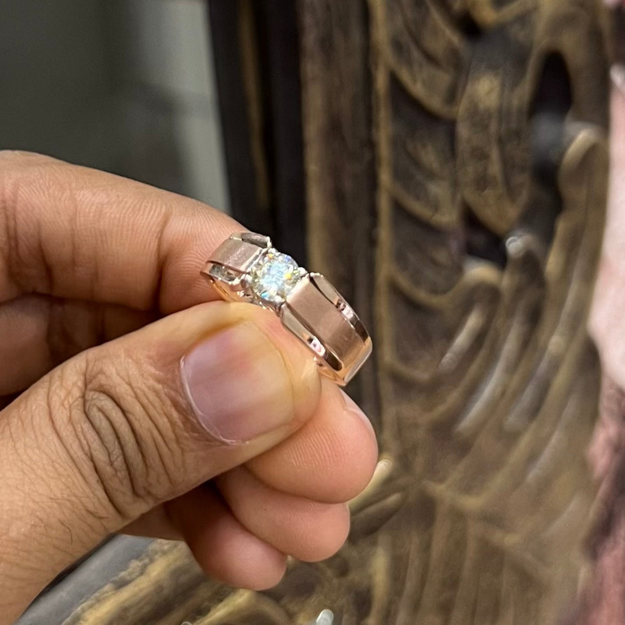A man's hand holding a diamond solitaire ring with a gold band.