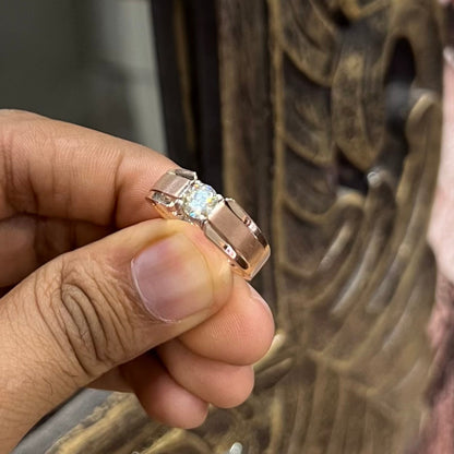 A man's hand holding a diamond solitaire ring with a gold band.