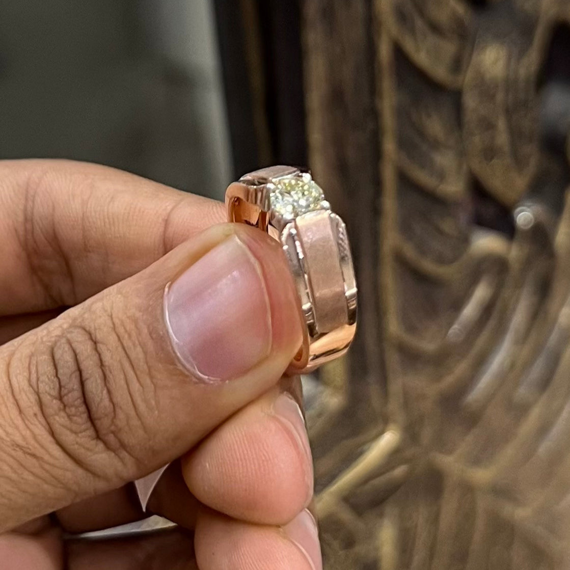 A man's hand holding a diamond solitaire ring with a gold band.