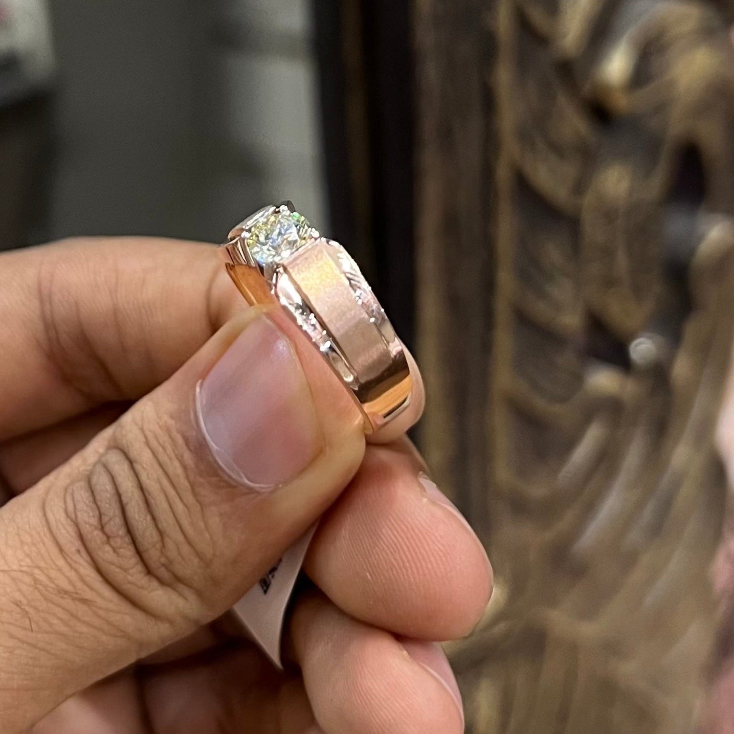 A man's hand holding a diamond solitaire ring with a gold band.